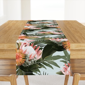 May include: A tropical floral table runner with pink and white protea flowers, orange and yellow flowers, and green leaves on a light blue background.