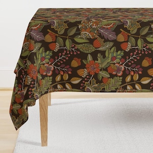 May include: A brown tablecloth with a floral pattern featuring red, orange, green, and yellow flowers, leaves, and acorns. The tablecloth is draped over a table with wooden legs.