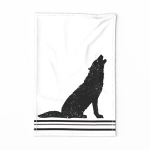 Puede incluir: Una toalla de cocina en blanco y negro con una silueta desgastada de un lobo aullando a la luna. La toalla tiene tres rayas negras en la parte inferior.