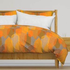 May include: A bed with a wooden headboard and a duvet cover with a geometric pattern in shades of orange, brown, and beige.