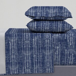 Op de afbeelding: Een blauwe en witte beddengoedset met twee bijpassende kussenslopen. Het laken heeft een subtiel, gestructureerd ontwerp met witte stiksels.