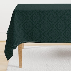 Pode incluir: Uma toalha de mesa verde escura com um padrão de damasco. A toalha de mesa está drapeada sobre uma mesa de madeira.