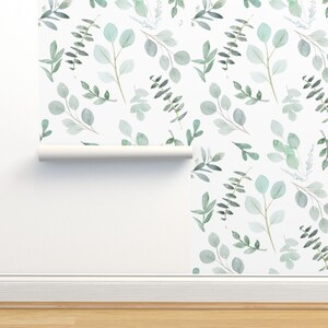 May include: A white background with a repeating pattern of green watercolour leaves and branches. The pattern is shown on a roll of wallpaper.