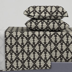 May include: A bedding set featuring two rectangular pillows and a flat sheet, all decorated with a repeating pattern of cream-colored moths and small stars set against a dark charcoal background, creating a consistent graphic design.