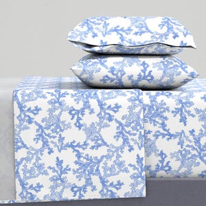 May include: A white bed sheet with a blue coral reef pattern. Two blue coral reef patterned pillowcases are stacked on top of the sheet.