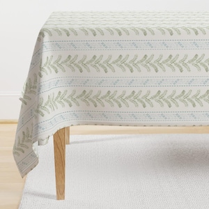 May include: A white tablecloth with a green and blue floral pattern. The tablecloth is draped over a wooden table.