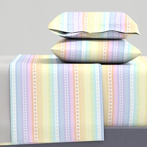 Könnte beinhalten: Ein Bettwäsche-Set mit pastellfarbenen Regenbogenstreifen und zwei passenden Kissenbezügen. Die Bettwäsche hat verschiedene pastellfarbene Streifen und Muster, darunter Punkte, Gingham und Streifen.