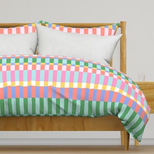 May include: A bed with a green, pink, blue and yellow checkered duvet cover. The duvet cover has a geometric pattern of stripes and squares.
