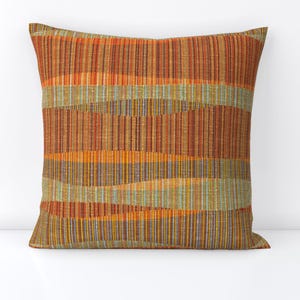 May include: A square throw pillow with a woven fabric cover. The fabric is a mix of orange, brown, yellow, and green stripes.