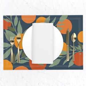 May include: A blue placemat with a white plate, gold silverware, and a white napkin. The placemat has a pattern of orange slices and green leaves.