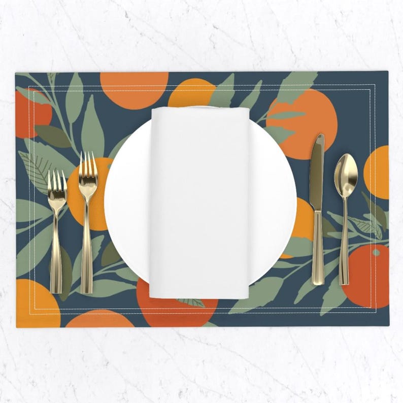 May include: A blue placemat with a white plate, gold silverware, and a white napkin. The placemat has a pattern of orange slices and green leaves.
