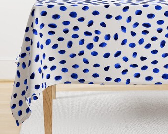 May include: White tablecloth with a blue watercolor polka dot pattern. The tablecloth is draped over a wooden table.