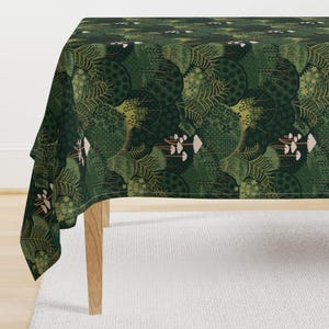 May include: A green tablecloth with a repeating pattern of stylized trees, ferns, and mushrooms. The design features various shades of green, with accents of beige and white. The tablecloth is draped over a wooden table.