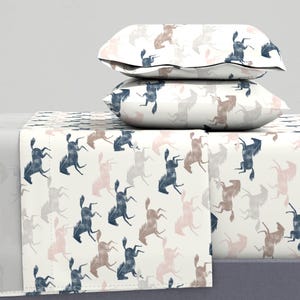Op de afbeelding: Een wit beddengoedset met een herhalend patroon van blauwe en roze paarden. De set bevat een plat laken, een hoeslaken en twee kussenslopen.