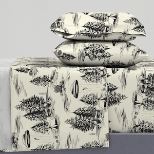 May include: A cream-colored bed sheet with a black and white print of trees and tents. Two matching pillowcases are stacked on top of the sheet.