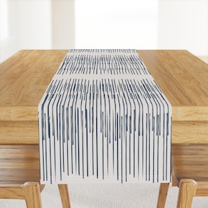 May include: A rectangular table runner featuring a cream backdrop and a design of navy blue vertical lines. The runner is laid on a wooden table, offering a contemporary aesthetic to the dining space.
