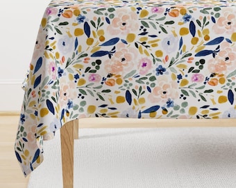 Op de afbeelding: Een wit tafelkleed met een bloemenpatroon in tinten roze, geel, blauw en groen. Het tafelkleed heeft een aquarelachtig ontwerp met kleine bloemen en bladeren.