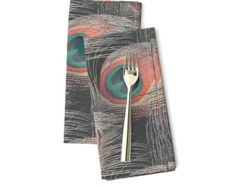 May include: Two black fabric napkins with a peacock feather pattern in shades of teal, pink, and white. The napkins are folded and placed on a white background.