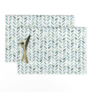 May include: Two placemats with a white background and a repeating pattern of green and blue watercolour leaves.