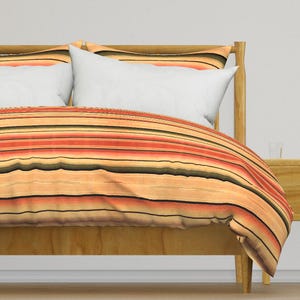 May include: A striped duvet cover in shades of orange, yellow, and brown. The duvet cover is on a wooden bed frame with two white pillows.