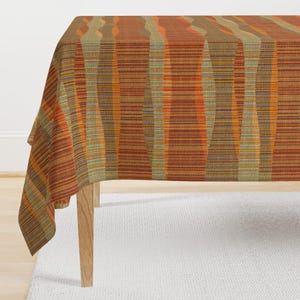 May include: A brown and orange striped tablecloth with a woven texture. The tablecloth is draped over a wooden table.