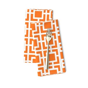 May include: Two orange and white geometric patterned napkins folded together with a silver fork on top.