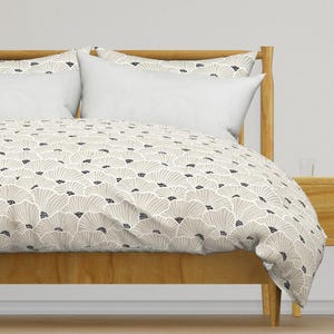 May include: A beige duvet cover with a white and black floral pattern. The duvet cover is on a wooden bed frame with two white pillows.
