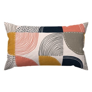May include: A rectangular pillow with a geometric pattern in shades of pink, yellow, gray, and blue. The pattern features curved lines, dots, and semi-circles.