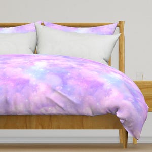 May include: A purple and blue galaxy print duvet cover with a white pillow on a wooden bed frame.