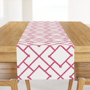 May include: A white table runner with a pink geometric pattern of intersecting lines. The pattern resembles a lattice or trellis.