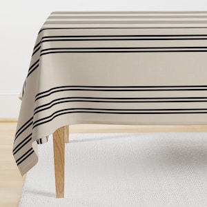 May include: A beige tablecloth with black stripes. The tablecloth is draped over a wooden table with a white rug underneath.