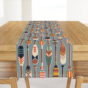 May include: A blue and white table runner with a repeating pattern of colorful paddles. The paddles have geometric designs in shades of red, orange, yellow, green, blue, and brown.