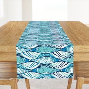 May include: A blue and white table runner with a repeating pattern of stylized fish swimming in waves. The fish are outlined in dark blue and have a light blue and white scale pattern.