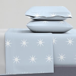 May include: A light blue bed sheet with a white starburst pattern. Two light blue pillowcases are stacked on top of the sheet.