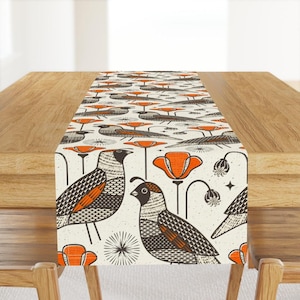 Peut inclure: Un chemin de table blanc avec un motif répété de coquelicots orange, de cailles noires et brunes et d'étoiles blanches. Le chemin de table est sur une table en bois.