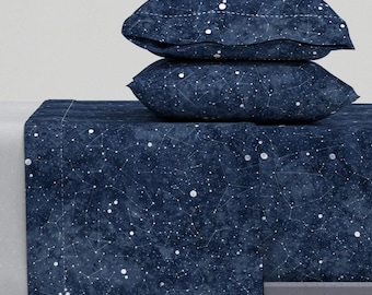 May include: A navy blue bedding set featuring a constellation pattern. The set includes a flat sheet, fitted sheet, and two pillowcases.