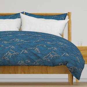 May include: A blue and white duvet cover with a wave pattern. The duvet cover is on a wooden bed frame.