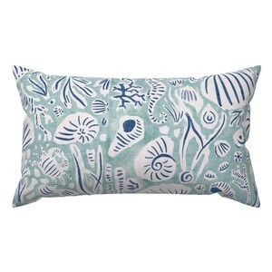 May include: Rectangular pillow with a sea-themed pattern. The pillow features a light teal background with white and navy blue illustrations of seashells, seahorses, and coral. The pillow has a soft, inviting appearance, perfect for coastal decor.