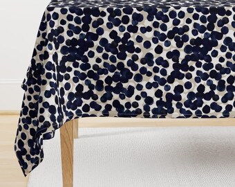 May include: A white tablecloth with a navy blue polka dot pattern. The tablecloth is draped over a wooden table.