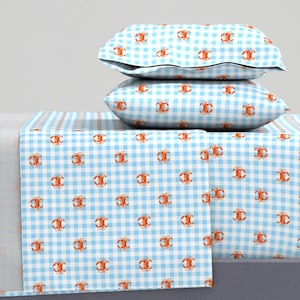 May include: A blue and white gingham patterned bedding set with a red crab design. The set includes a flat sheet, fitted sheet, and two pillowcases.
