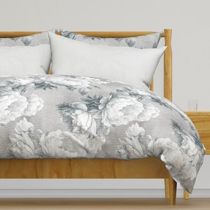 May include: A grey and white floral duvet cover with a subtle linen texture. The duvet cover is on a wooden bed frame with a white pillow.