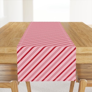 Puede incluir: Un camino de mesa a rayas rosa y rojo con un patrón diagonal. El camino de mesa está sobre una mesa de madera.