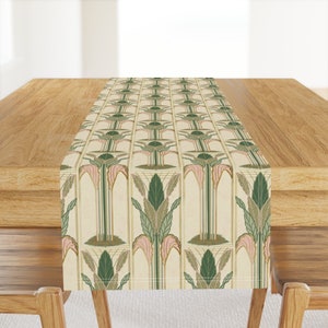 May include: A beige table runner with a repeating pattern of stylized green palm trees with pink accents. The pattern is on a cream background.