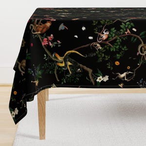 May include: Black tablecloth with a repeating pattern of monkeys, flowers, and leaves. The monkeys are in various poses, some are swinging from branches, others are sitting on leaves. The flowers are in shades of pink and white. The leaves are green and brown.