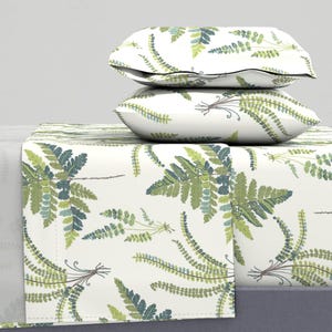 Puede incluir: Una sábana blanca con un patrón de helechos verdes. Dos fundas de almohada blancas con el mismo patrón de helechos están apiladas encima de la sábana.