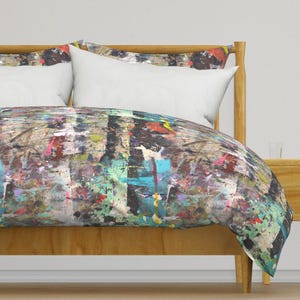 Puede incluir: Una funda nórdica con un diseño abstracto de salpicaduras de pintura en tonos de azul, verde, rojo, amarillo y negro. La funda nórdica está sobre un marco de cama de madera.