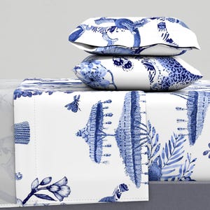 May include: A white bedding set with a blue and white floral pattern. The bedding set includes a flat sheet, fitted sheet, and two pillowcases. The pattern features a variety of flowers, leaves, and other botanical elements. The bedding set is made of a soft, comfortable fabric.
