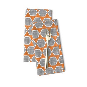 May include: Two orange and gray geometric patterned cloth napkins folded together. The napkins have a woven texture and a white outline around the geometric shapes.