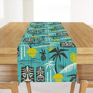 May include: A turquoise table runner with a repeating pattern of tiki masks, palm trees, pineapples, and suns. The pattern is in black, white, and yellow.