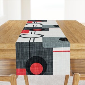 Puede incluir: Un camino de mesa geométrico negro, blanco, rojo y gris con un diseño moderno. El camino de mesa está hecho de una tela texturizada y presenta círculos, cuadrados y líneas.